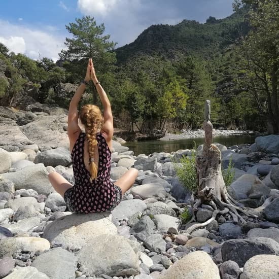 Femme méditant en position de yoga sur des galets au bord d'une rivière de montagne